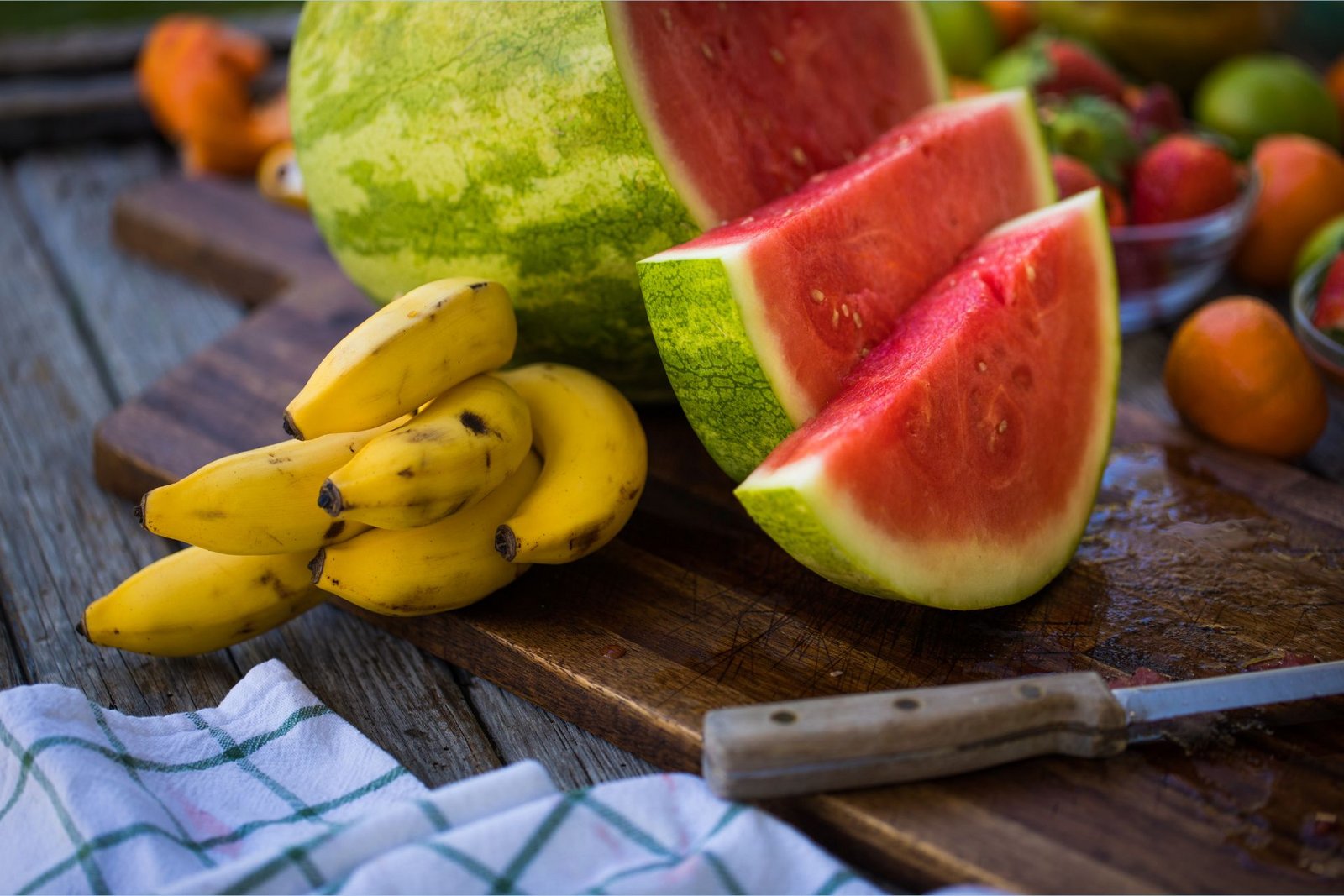 Plátanos ricos en potasio junto a una sandía en rodajas rica en L-citrulina sobre una tabla de cortar.